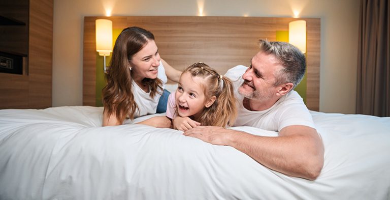 Happy family embracing while lying on bed in hotel room