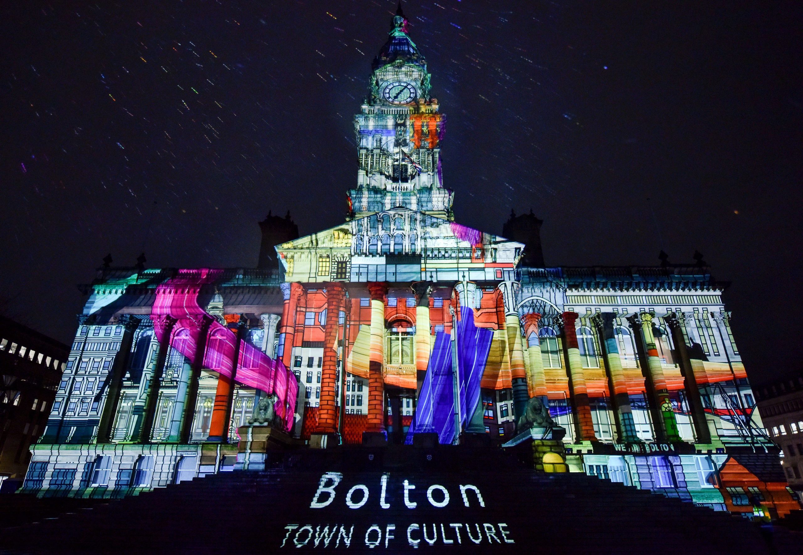 Image of Bolton Town Hall lit up in colourful lights, words say 'Bolton Town of Culture'