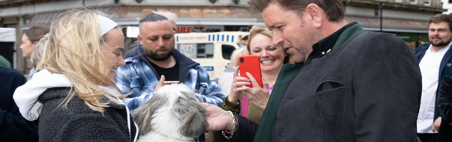 A person holding a dog whilst James Martin strokes it